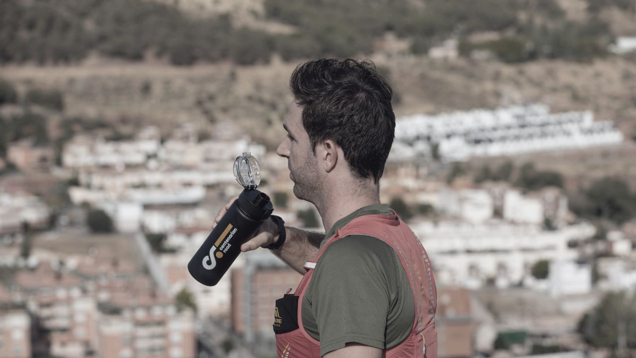 hombre bebiendo de botella de centenarian road con ciudad de fondo